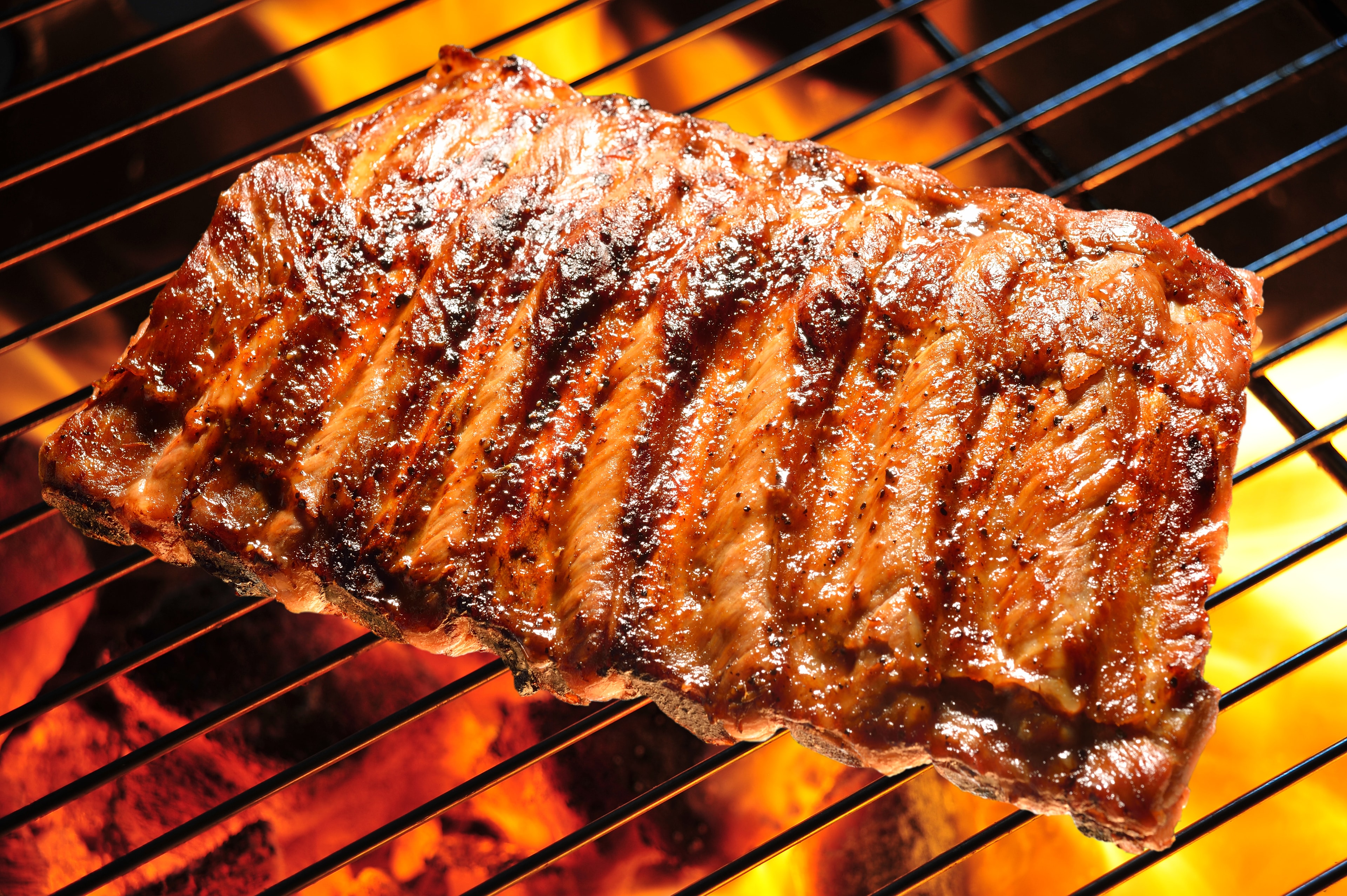 Baby back pork ribs sizzling on an open flame grill with beautiful char marks